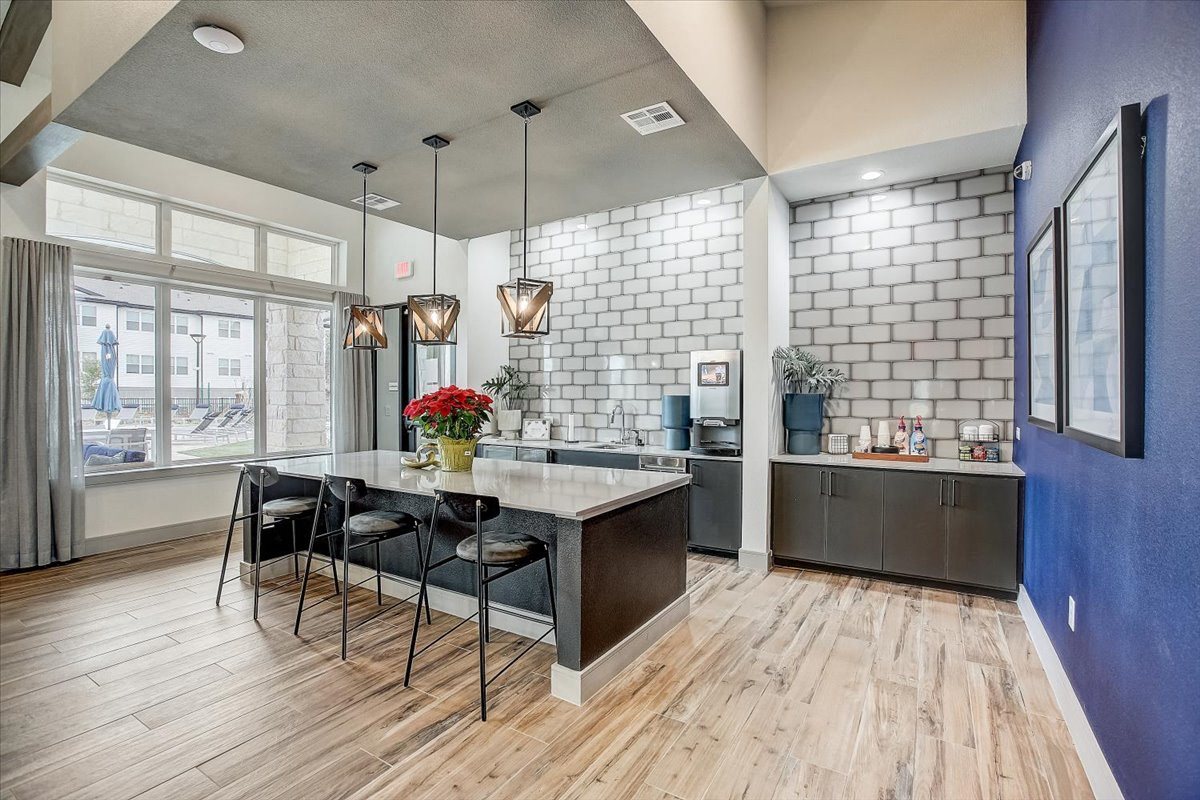 Shared clubhouse kitchen with expansive island seating, sleek cabinetry, and tall windows for daylight.